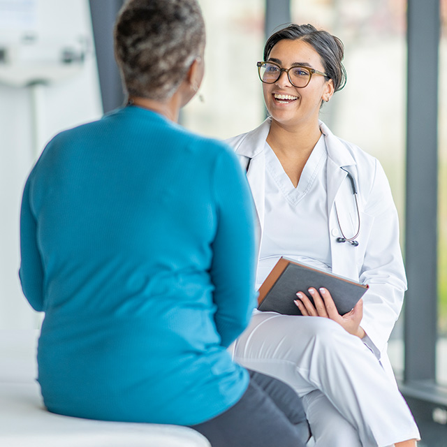 A clinician speaking with a patient. She is holding a clipboard in her hand.