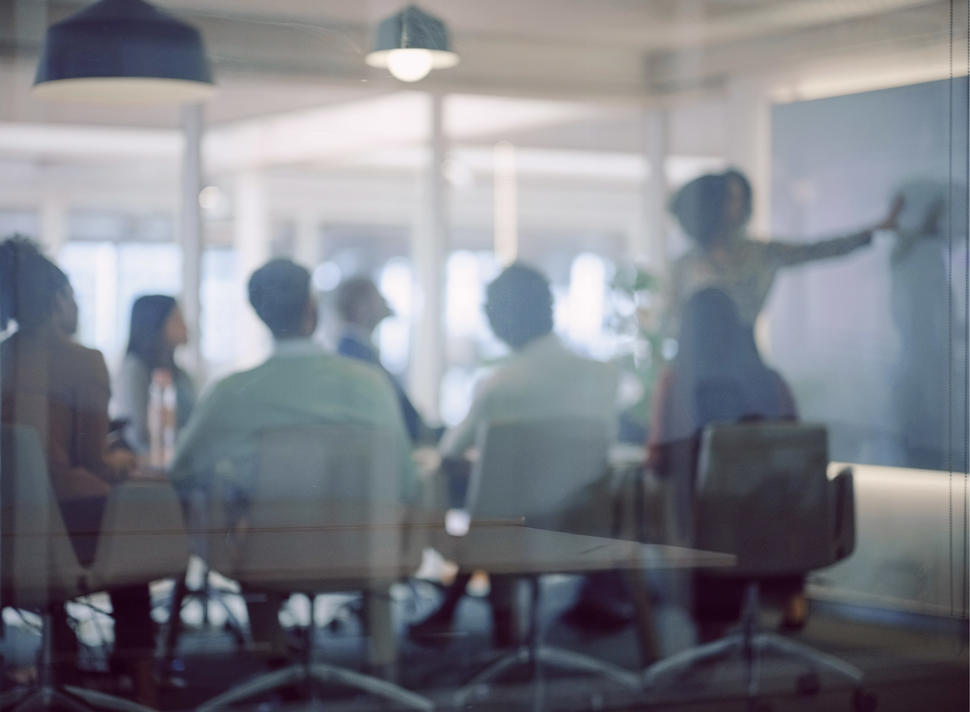 An employee writes on a blackboard as seated colleagues watch