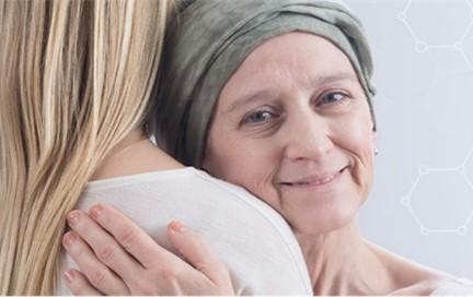 A caregiver is embracing a cancer patient who is wearing a headscarf.