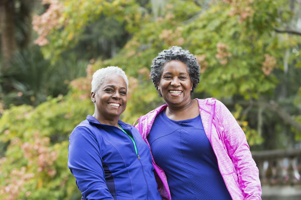 Two happy women standing in front of green trees