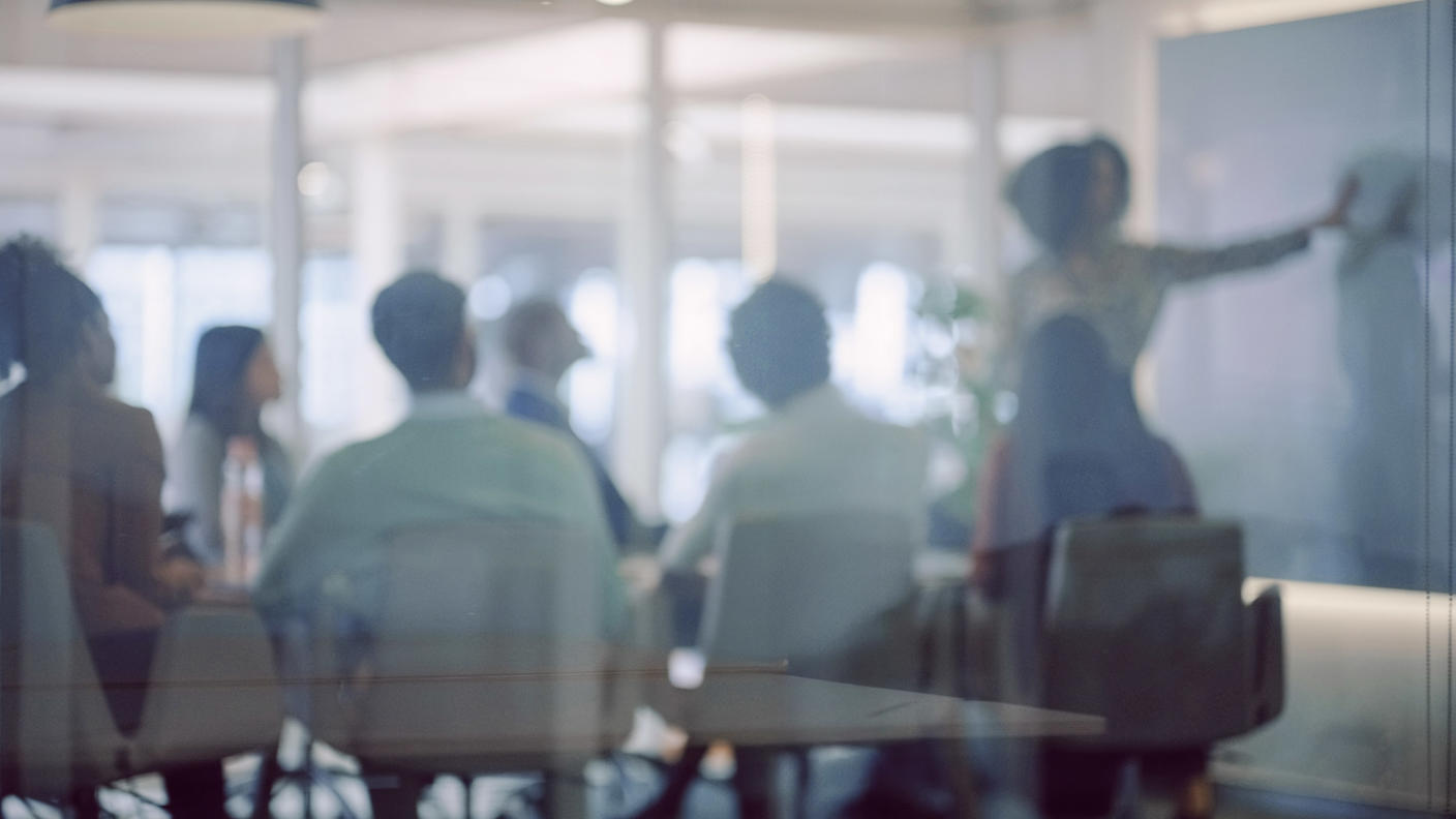 An employee writes on a blackboard as seated colleagues watch