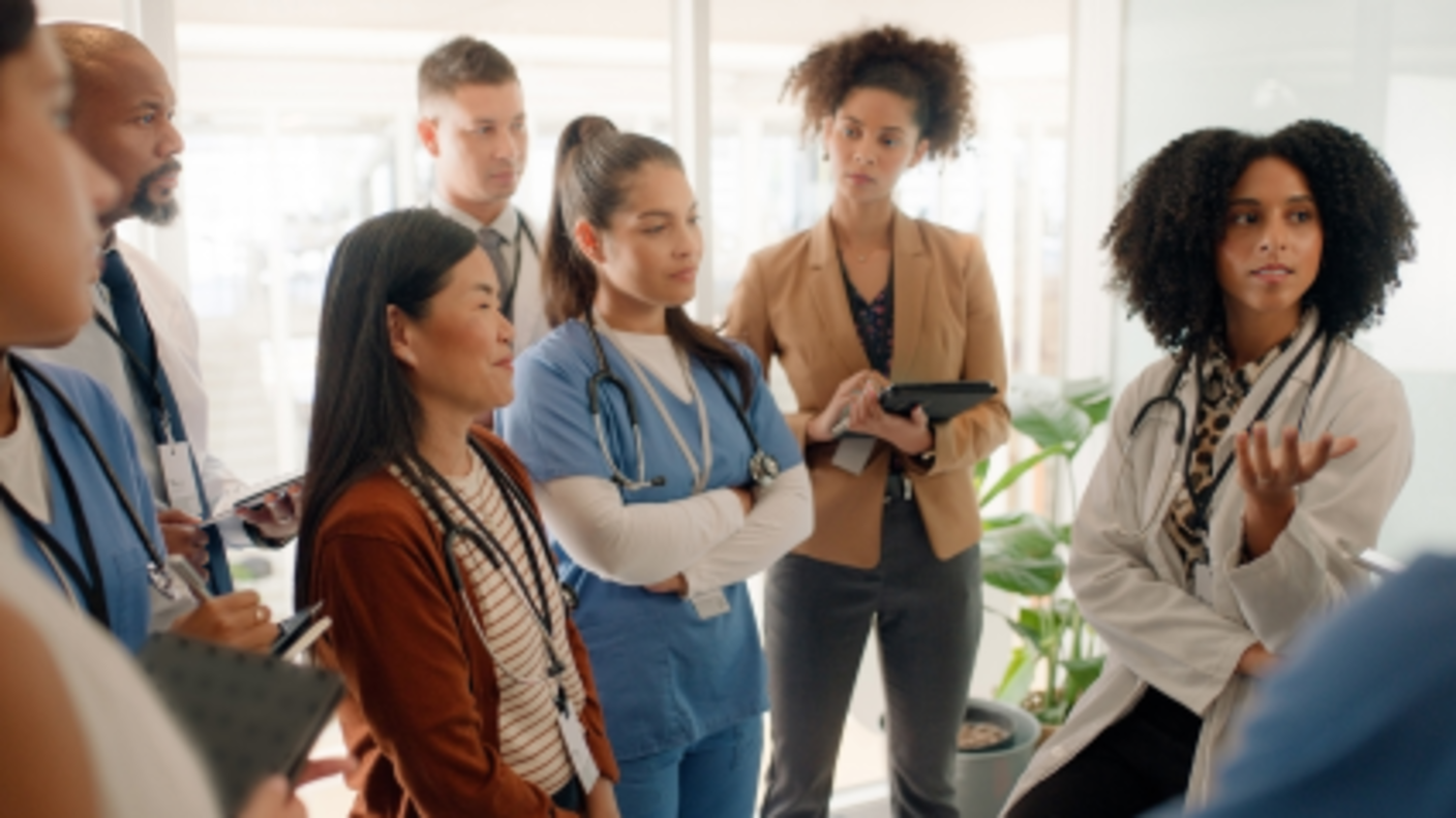A diverse group of medical professionals and research staff have a standing meeting