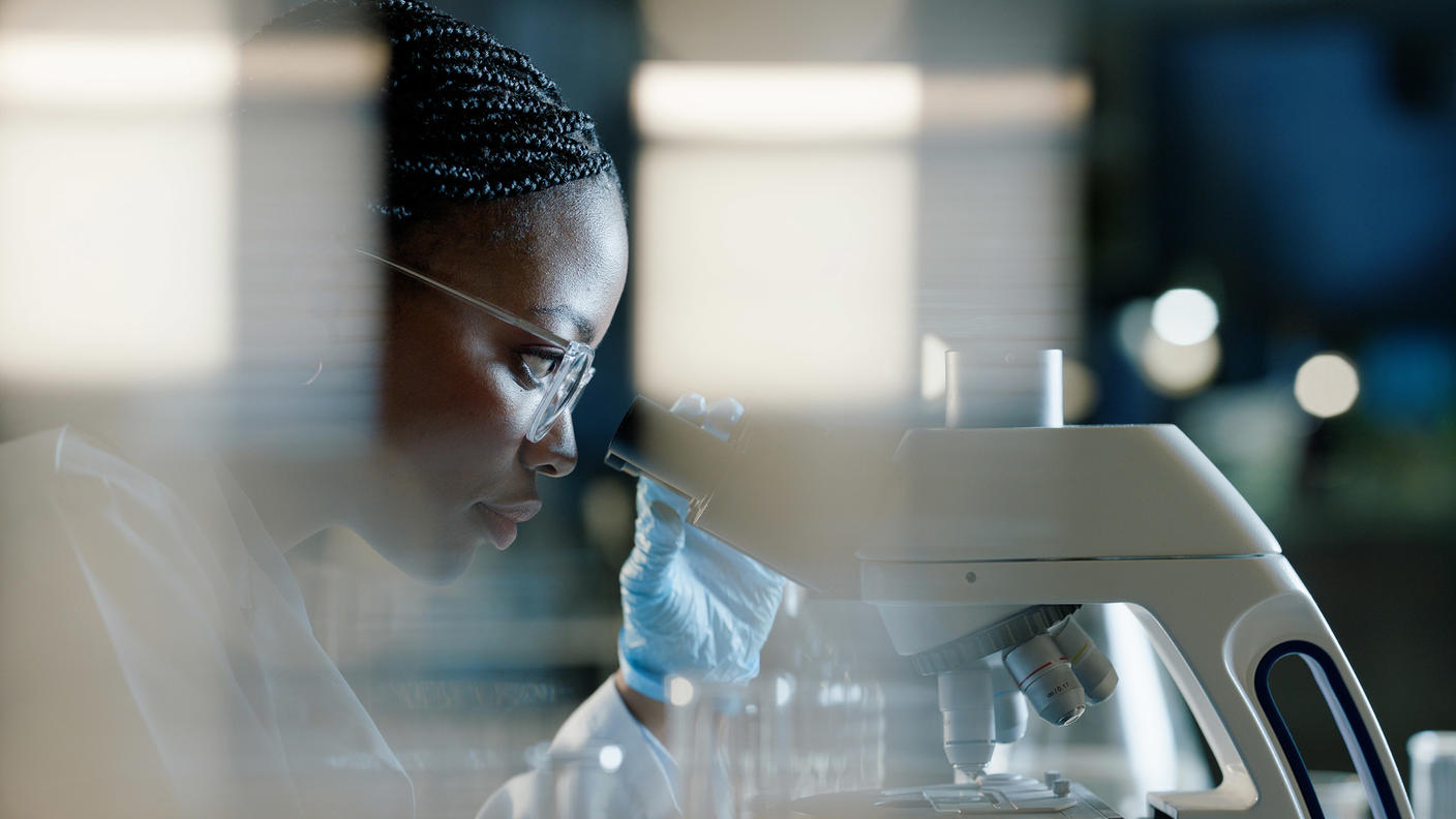 A female scientist is sitting in front of and looking into a microscope