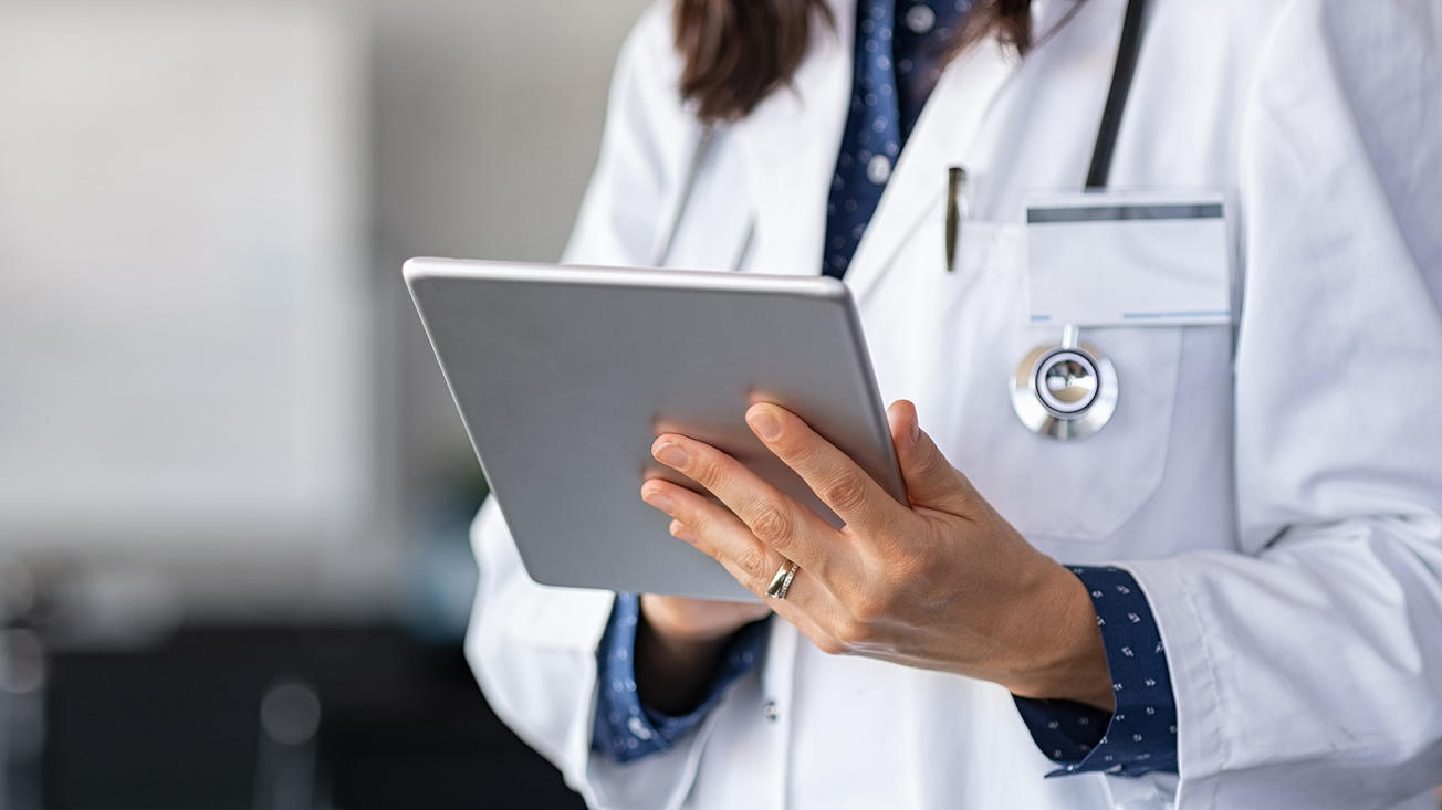 A medical professional in a lab coat is holding a tablet