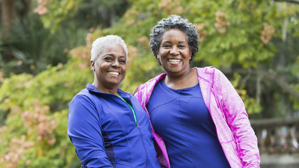 Two happy women standing in front of green trees